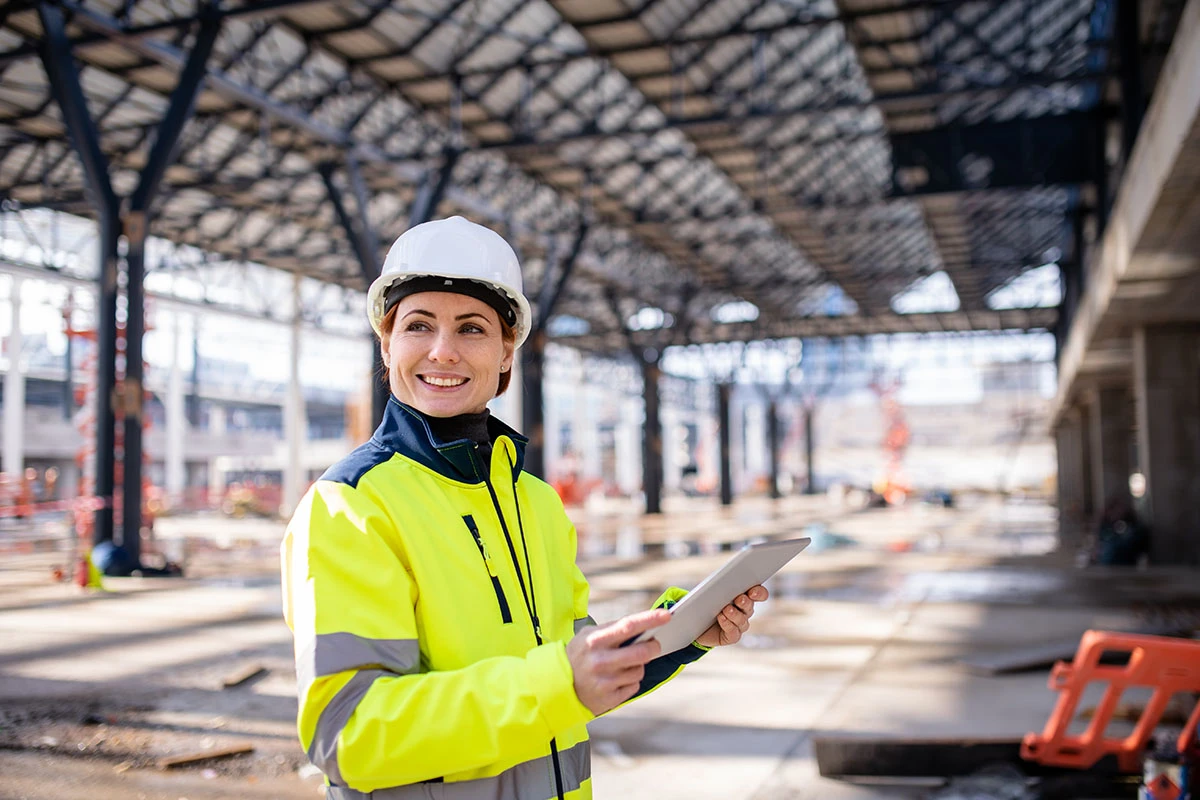 Kontrolleurin in Warnjacke und Helm in einer Hallenbaustelle