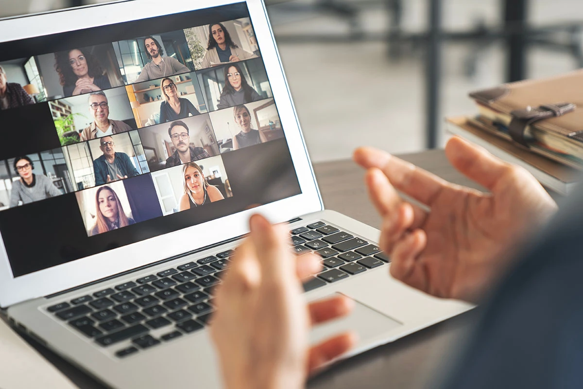 Aufgeklappter Laptop auf dem ein Meeting mit vielen Personen zu ist fotografiert aus der Ich-Perspektive