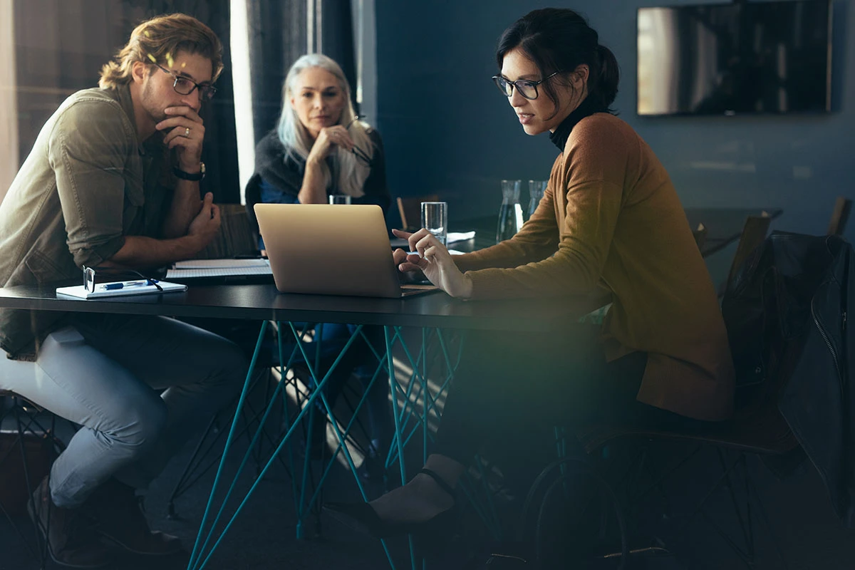 Drei Menschen arbeiten zusammen und schauen sich in einem modernen B&uuml;ro eine Pr&auml;sentation auf einem Laptop an