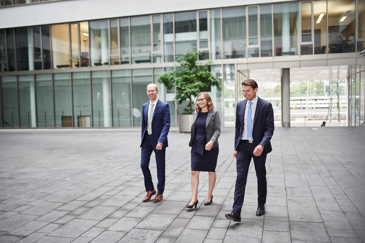 Das dreiköpfibe Leitungsteam der SüdFactoring GmbH schreitet über den Platz vor dem Firmengebäude